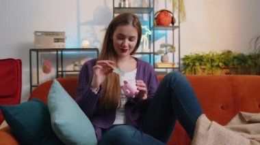 Poor young woman insufficient amount of money, holding piggybank and one dollar banknote at home apartment. Financial crisis. Bankruptcy. Poverty and destitution. Girl in living room sitting on sofa