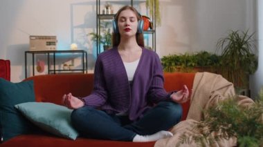 Keep calm down, relax, inner balance. Portrait of woman breathes deeply with mudra gesture, eyes closed, meditating with concentrated thoughts, peaceful mind at home apartment. Girl sitting on couch