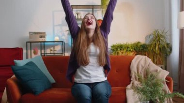 Money cash dollar rain falling on woman celebrating success, winning, goal achievement, good news, lottery jackpot luck, dream come true at home apartment indoors. Career grow. Girl sits on sofa