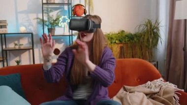 Portrait of woman using virtual reality futuristic technology VR app headset helmet to play simulation 3D 360 video game, watching film movie at modern home apartment. Girl in goggles sitting on couch