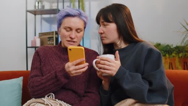两个快乐的女人 女同性恋者或朋友 在家里客厅的电子商务平台上使用智能手机购物 在一起浏览各种社交媒体应用程序时 他们都会体验到乐趣和乐趣 — 图库视频影像