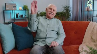 Hoş geldiniz. Büyükbaba kameraya dostça gülümseyen, el sallayan merhaba diyen selam veren, selamlayan ya da hoşça kal diyen, evde misafirperver bir yüz ifadesiyle karşılayan yaşlı adam. Oturma odasındaki kanepede oturan yaşlı adam.