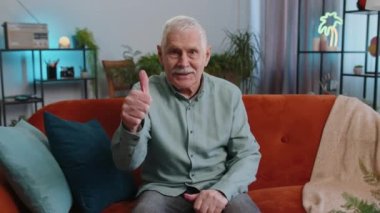 Gibi. Mutlu, kıdemli büyükbaba onaylayıcı bir şekilde kameraya bakıyor olumlu bir şey imzalıyor, iyi haber, olumlu geri bildirim gibi. Sınıftaki kanepede oturan yaşlı adam.