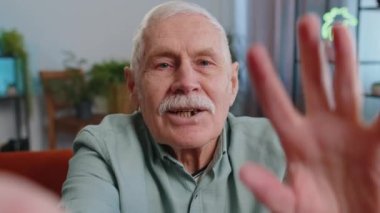 Üst düzey büyükbabanın internetteki selfie görüntülerini çekerken el sallayarak evin içinde kameraya bakarken görüntüsü. İletişim, toplantı. Yaşlı blogcu akıllı telefon konuşması yapıyor