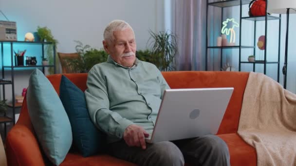 爷爷老年人坐在沙发上看着手提电脑摄像头 和朋友或家人一起做视频摄像头电话会议 享受着愉快的对话 上了年纪的人在家里笑着打招呼 — 图库视频影像