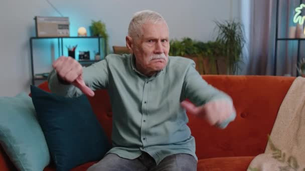 嫌いだ 親指のサインジェスチャーを示す動揺の高齢者の祖父の男は 現代の家庭のアパート内で不満不満悪い仕事を表現します 不満な高齢者男で部屋にソファ — ストック動画