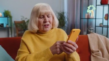 Hüzünlü yaşlı büyükanne akıllı telefon daktilo kullanıyor, beklenmedik piyango sonuçlarını kaybediyor, kötü haber, servet kaybı, son teslim tarihi, virüs, borç. Kanepede oturan yaşlı kadın.