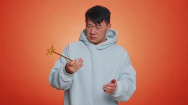 Magician wizard man gesturing with magic wand fairy stick, making wish come true, casting magician spell, advertising holidays sale discount. Handsome asian guy isolated on orange studio background