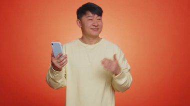 Asyalı mutlu adam akıllı telefonu boş bir yeri işaret ediyor, reklam alanı ticari metin, mobil uygulama, promosyon fotokopi alanı, kablosuz telefon bağlantısı 5G öneriyor. Yakışıklı Çinli adam.