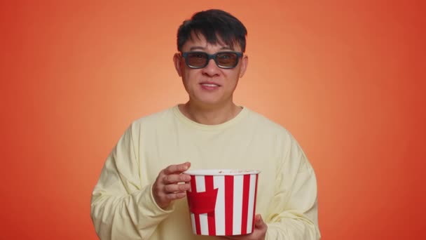 3Dメガネでポップコーンを食べ 興味深いテレビシリーズ スポーツゲーム オンラインソーシャルメディア映画コンテンツを見て興奮したアジア人男性 幸せな男楽しんで国内エンターテイメント上のオレンジ背景 — ストック動画