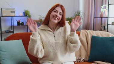 Hoş geldiniz. Kızıl saçlı kadın kameraya dostça gülümsüyor ve el sallıyor merhaba, merhaba, merhaba ya da güle güle, evde misafirperver bir yüz ifadesiyle karşılıyor. Oturma odasındaki kanepede oturan kızın portresi.