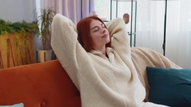 Yorgun genç bir kadının portresi evdeki kanepede dinlenmenin keyfini çıkarıyor. Mutlu kızıl kız kanepede uzanmış dinleniyor yorucu bir günün ardından kestiriyor gözlerini kapatıyor, ellerini başının arkasına koyuyor stresten kurtuluyor, dinleniyor.