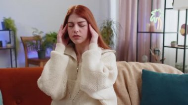 Baş ağrısı problemini tedavi etmek için tapınakları ovuşturan hoşnutsuz genç bir kadın, tansiyon ve migrenden muzdarip, evde acı içinde kıvranan yüksek tansiyon. Kız kanepeye oturur. Yaşam Tarzları