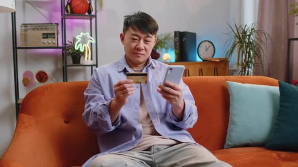 亚洲人在汇款 网上购物 在家里订购食物时使用信用卡和智能手机 快乐的中国人坐在客厅的沙发上 — 图库视频影像