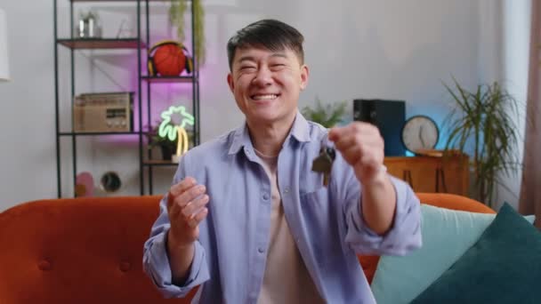 亚洲人房地产经纪人举起手 展示新住房公寓的钥匙 购买或租赁房产 在室内现代住房公寓的抵押贷款 房间里的中国人坐在沙发上 — 图库视频影像