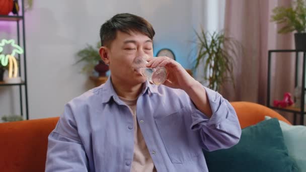 天然のアクアのガラスを保持している喉の渇きアジアの男性は 家のリビングルームに脱水症状が座って防ぐために まだ水を飲む船を作る 良い生活習慣 健康的な痩身 減量の概念を持つ中国の男 — ストック動画