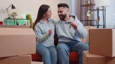Genç bir aile çifti olan erkek, yeni ev dairesinin anahtarlarını göstererek el kaldırıyor, gayrimenkul alıyor ya da kiralıyor, ev kredisi kullanıyor. Karı koca kanepede yan yana.