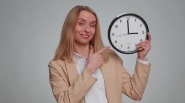 Senin sıran. Duvardaki ofis saatinde zamanını gösteren genç bir iş kadınının portresi, tamam, başparmağınızı kaldırın, onaylayın, kamerayı işaret edin. Resmi takım elbiseli bir kadın. Gri stüdyo geçmişi olan güzel bir kadın.
