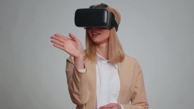 İş kadını, çevrimiçi oyun uygulaması oynamak için kulaklık kullanıyor. Sanal gerçeklik 3D 360 video içeriği izliyor. Stüdyonun gri arka planında gözlüklü bir kız izole edilmiş. Gelecekçi teknoloji