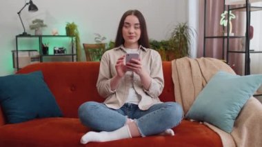 Kanepede oturan genç bir kadının portresi evde gülümseyen bir cep telefonu kullanıyor. Akıllı telefon sosyal medya uygulamaları üzerinden rahatlama filmi izlerken mesajları paylaşan kız