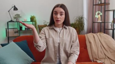 Face palm. Shame on you. Upset woman making disrespect gesture, feeling bored, disappointed in fail results bad news. Portrait of girl at home apartment living room sitting on orange couch. Lifestyles