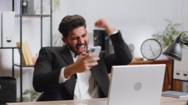 Akıllı telefon üzerinde çalışan mutlu Hintli genç işadamı piyango kazanan bir galibiyet oyunuyla şok oldu. Kariyer başarısı var. Heyecanlı sakallı Hintli adam ev ofisinde serbest çalışıyor.