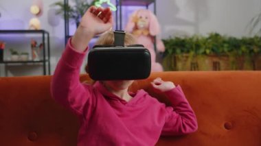 Genç sarışın çocuk modern sanal gerçeklik fütüristik teknoloji VR uygulama kulaklığı kullanarak 3D video oyunu simülasyonu yapıyor, film izliyor. Evde oturan genç bir kız çocuk kanepede oturuyor.