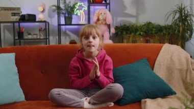 Çocuk kız bağırıyor, başarıyı kutluyor, kazanıyor, gol başarısı, iyi haber, el hareketleriyle yumruk kaldırıyor. Başardım, piyango şansı. Genç bir kız evde oyun oynuyor oturma odasında kanepede oturuyor.