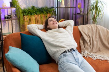 Yorgun genç bir kadının portresi evdeki kanepede dinlenmenin keyfini çıkarıyor. Mutlu güzel kız kanepede uzanmış dinleniyor yorucu bir günün ardından kestiriyor gözlerini kapatıyor, ellerini başının arkasına koyuyor, stresten kurtuluyor, dinleniyor.