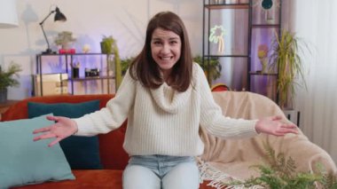 What. Why. Woman raising hands in indignant expression asking reason of failure demonstrating disbelief irritation by troubles at modern home apartment. Portrait of girl in living room sitting on sofa