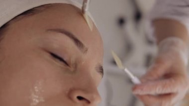 Enzim terapisi. Güzellik uzmanı orta yaşlı bir kadının alnına fırçayla nemlendirici krem maske takıyor. Kız cilt bakımı spa prosedürü. Yüz kozmetolojisi tedavisi. Dikey çekim