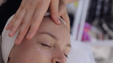 Terapist kadın rahatlatıcı spa yüz masajını elleriyle yaptırıyor. Kuaförde pürüzsüz, sağlıklı cilt bakımı. Detoks ve iyileşme. Yüz fizyolojisi seansında müşteri. Dikey çekim