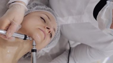 Güzellik uzmanı kadınlara mikro akım yaptırıyor. Spa kliniğinde anti-yaş kız cilt bakımı. Kozmetik doktoru çene estetik güzellik tedavisi için elektriksel impulslar kullanıyor. Dikey görünüm