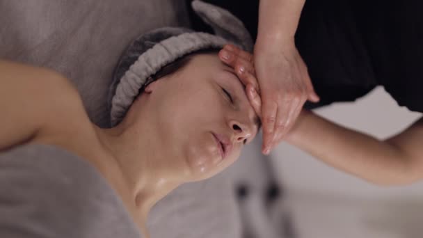 美容師カイロプラクターは 女性がスパの顔マッサージをリラックスさせ 頭を持ち上げる練習を呼吸する クライアントの女の子額に手を握っている女性医師 美容室で化粧品の手順 — ストック動画