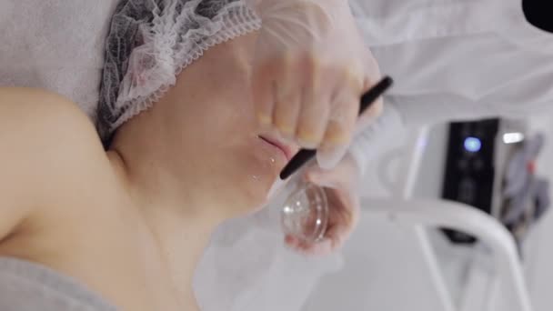 酶的治疗 美容师在中年妇女的额头上用刷子涂上保湿的医用剥皮膏面膜 女孩皮肤护理温泉程序 面部美容术治疗 垂直射击 — 图库视频影像