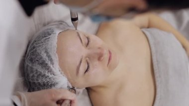 Kozmetik doktoru kadınlara mikro akım tedavisi uyguluyor. Kız cilt bakımı anti-yaş spa prosedürü. Güzellik uzmanı, yüz kozmetik güzellik tedavisi için elektriksel impulslar kullanıyor. Dikey görünüm