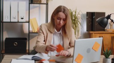Tired exhausted young businesswoman working on laptop at office with many sticker task inscriptions. Freelancer woman busy occupation feels sad boredom overworked multitasking. Panic attack, deadline