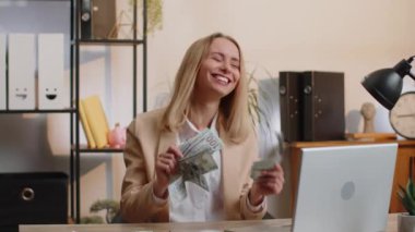 Nakit para banknotlarının hayranı olan genç bir iş kadını kutlama, dans, başarı kariyeri, piyango oyunu galibi, büyük gelir, ofis çalışma masasında zenginlik. Uzak çalışma