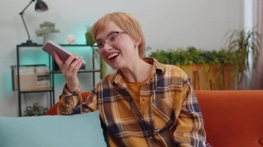 Kanepede oturan bir arkadaşla telefon konuşması yapan genç bir kadının portresi. Mobil akıllı telefon hoparlörlerinden hoşlanan mutlu bir kız modern ev oturma odasında içeride konuşuyor.