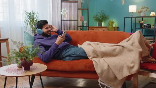 Happy Overjoyed Hindu Indian Man Wireless Headphones Relaxing Sits Couch — Vídeo de Stock