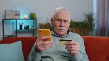 Büyükbaba kredi kartı ve akıllı telefon kullanarak para transfer ediyor, internetten nakit para almıyor, yemek siparişi veriyor, ev içinde faturaları ödüyor. Kanepedeki yaşlı adam.