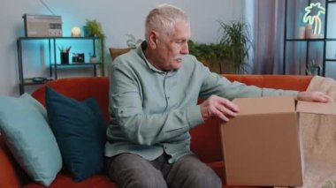 Mutlu son sınıf dede teslimat paketini boşaltan adam evde oturuyor. Gülümseyen yaşlı adam alışverişci, çevrimiçi dükkan müşterisi karton kutu açıyor hızlı posta gönderiminden satın alma hediyesi alıyor