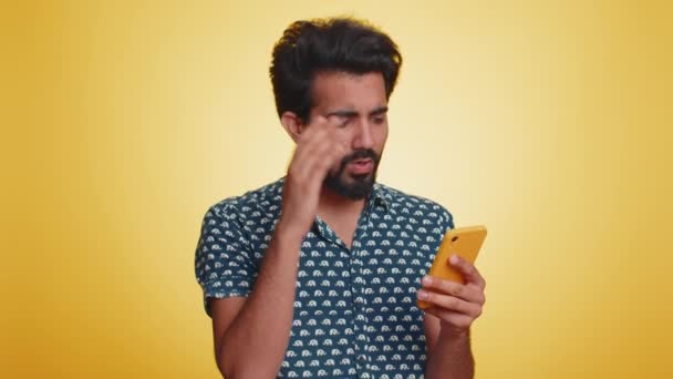 インド人の男性は 携帯電話の携帯電話の入力のブラウジングを使用すると 突然宝くじの結果 失敗に驚いて失う 黄色のスタジオの壁の背景に一人で隔離されたハンサムなHindu男 — ストック動画