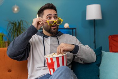 Üç boyutlu gözlüklü heyecanlı genç adam kanepede oturup patlamış mısır yiyor ve TV 'de ilginç bir spor oyunu izliyor, evdeki sosyal medya içeriğini filme çekiyor. Eğlenen adam