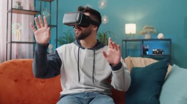 Sanal gerçeklik teknolojisi VR uygulama kulaklığı kullanarak 3D video oyunu simülasyonu izlemek için heyecanlı bir adam. Modern ev dairesindeki kanepede gözlüklü bir adamın portresi.
