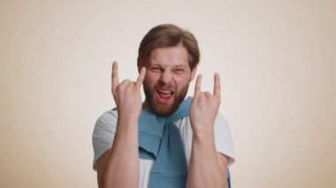 Coşkulu beyaz adam rock n roll hareketini elleriyle sergiliyor, havalı bir işaret, çılgın bir ifadeyle evet diye bağırıyor, dans ediyor, duygusal olarak başarıyla seviniyor. Genç mutlu adam bej arka planda izole
