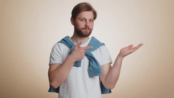 白人男子竖起大拇指 指向空旷的地方 商业广告区 复制空间为商品促销 在米色工作室背景下被隔离的年轻大胡子男人 — 图库视频影像