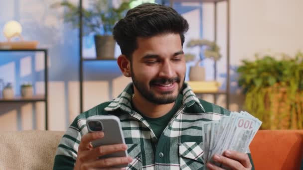 规划家庭预算 微笑的印度人数钱 用智能手机计算家里的账单 快乐的后来者满足于收入 并为计划的假期 礼物存钱 — 图库视频影像