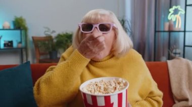 Kanepede 3 boyutlu gözlüklü büyükannem patlamış mısır yiyor ve evde ilginç TV dizileri, spor oyunları, filmler, çevrimiçi sosyal medya filmi içerikleri izliyor. Kıdemli kadın eğleniyor.
