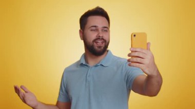 Mutlu Kafkas erkek gezgin blogcu, akıllı telefondan selfie çekiyor, aile veya arkadaşlarla çevrimiçi video görüşmesi yapıyor, canlı çeviri akışı yapıyor. Sarı arka planda, kapalı alanda izole edilmiş yakışıklı adam.